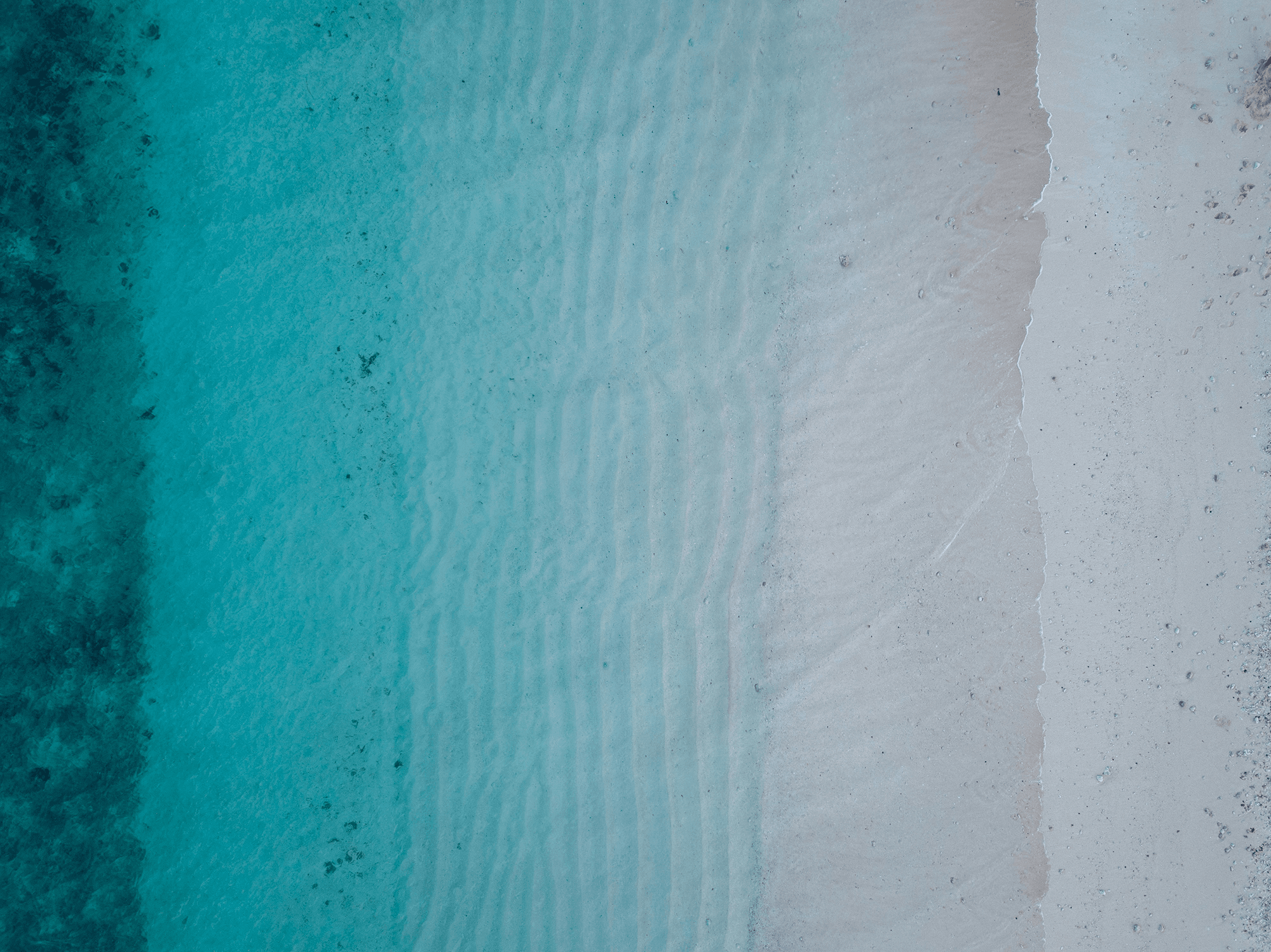 Aerial view of sand ripples beneath the water at a beach.
