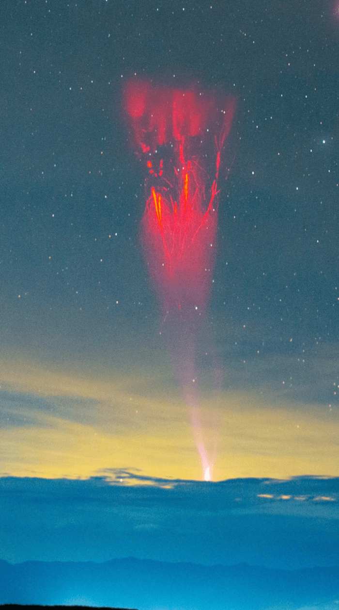 A gigantic jet rises from a distant thunderstorm into the ionosphere, where is splits into red streamers.