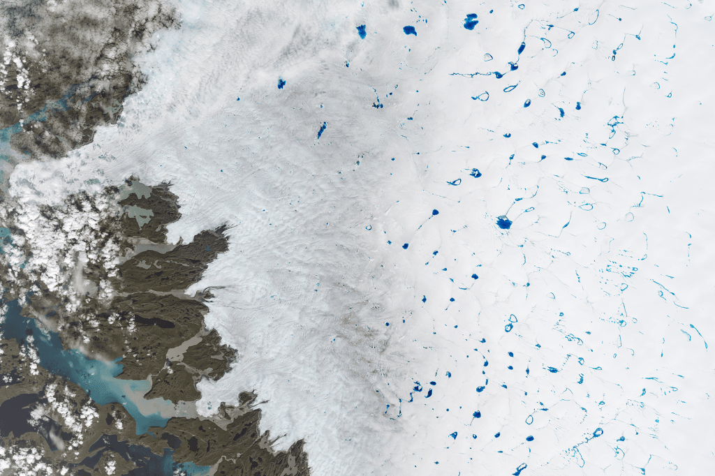 A satellite image of Greenland's ice sheet, showing jewel-toned blue meltwater ponds to the right, a haze of dirty ice in the center, and bare rock and open water to the left.