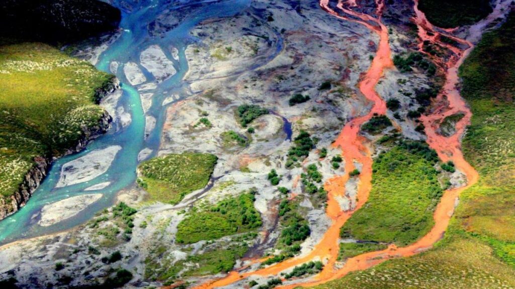 A contaminated portion of the Kutuk River runs orange alongside an uncontaminated portion of the same waterway.