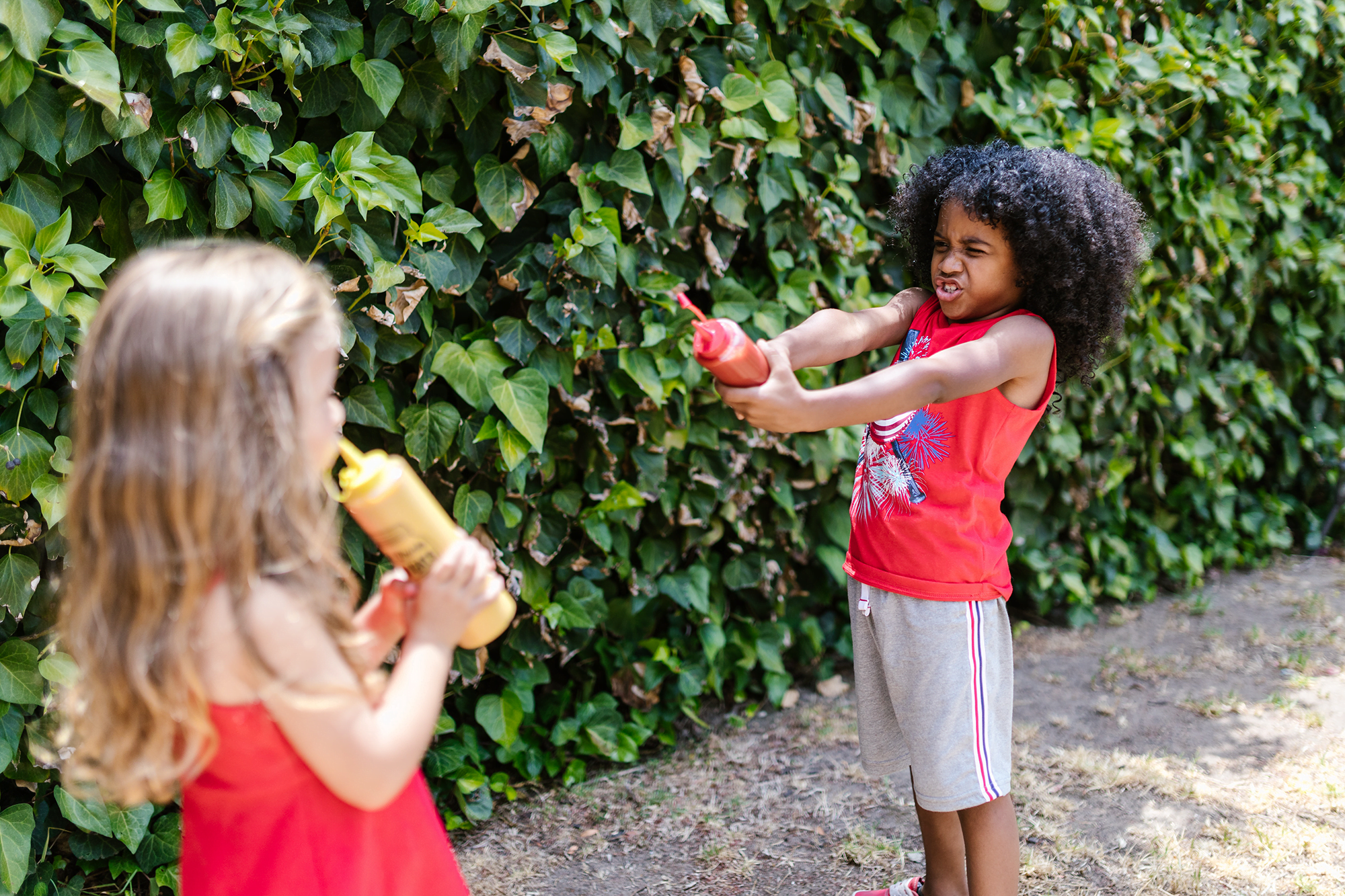 Two children playing with squeeze bottles of condiments.