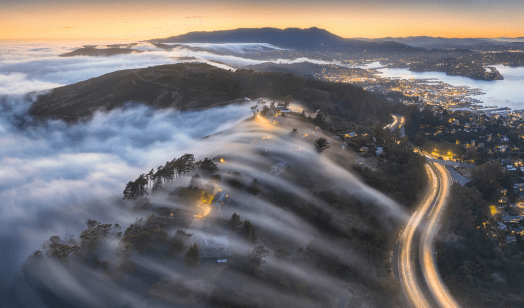Tendrils of fog flow over a hill crest at sunset.