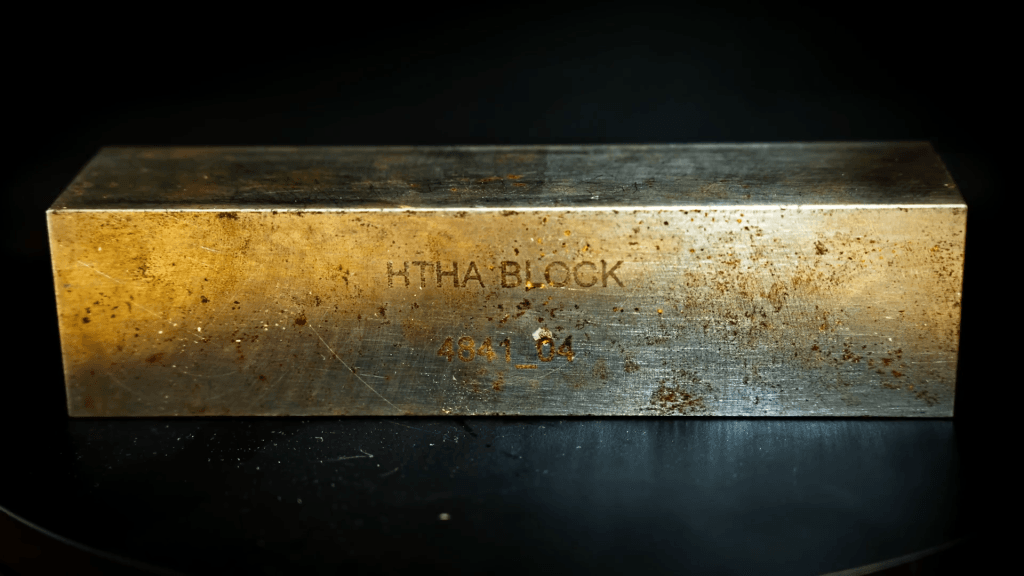 A rectangular block of steel with signs of oxidation/rusting.
