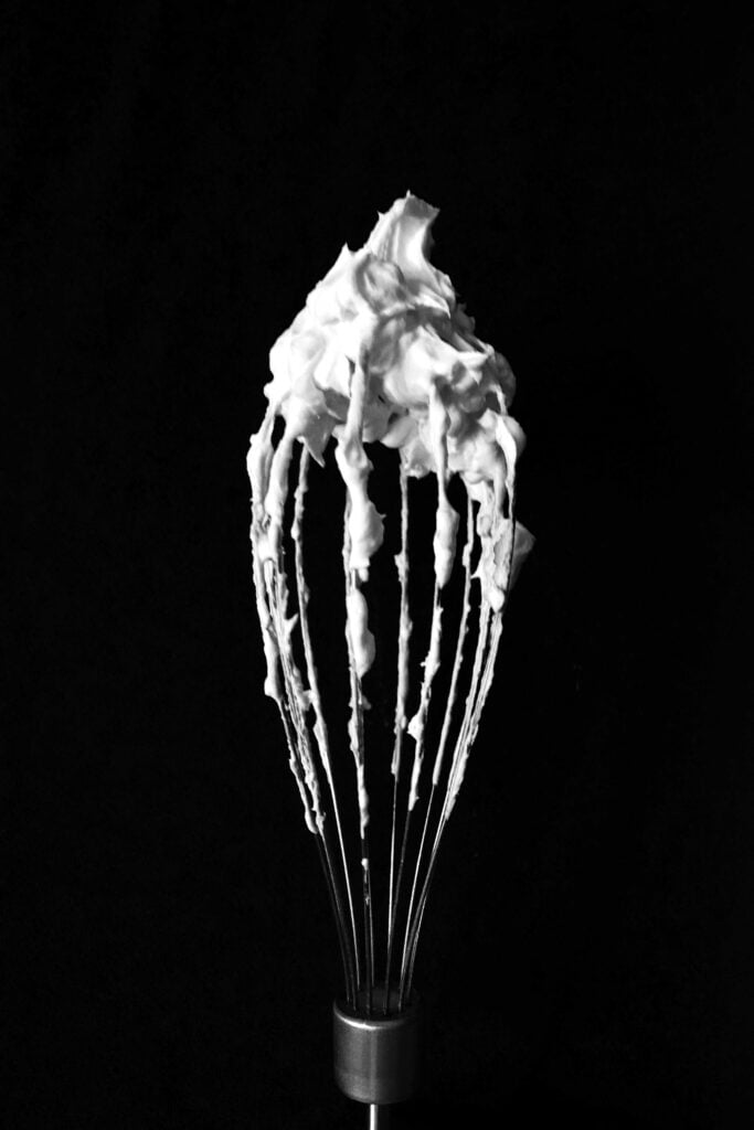 Whipped cream, a foam, clings to a whisk.