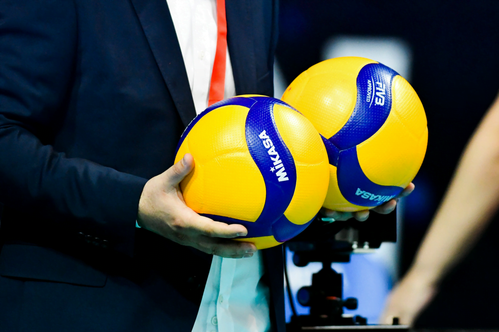 An official holds two dimpled competition indoor volleyballs. An official holds two dimpled competition indoor volleyballs.
